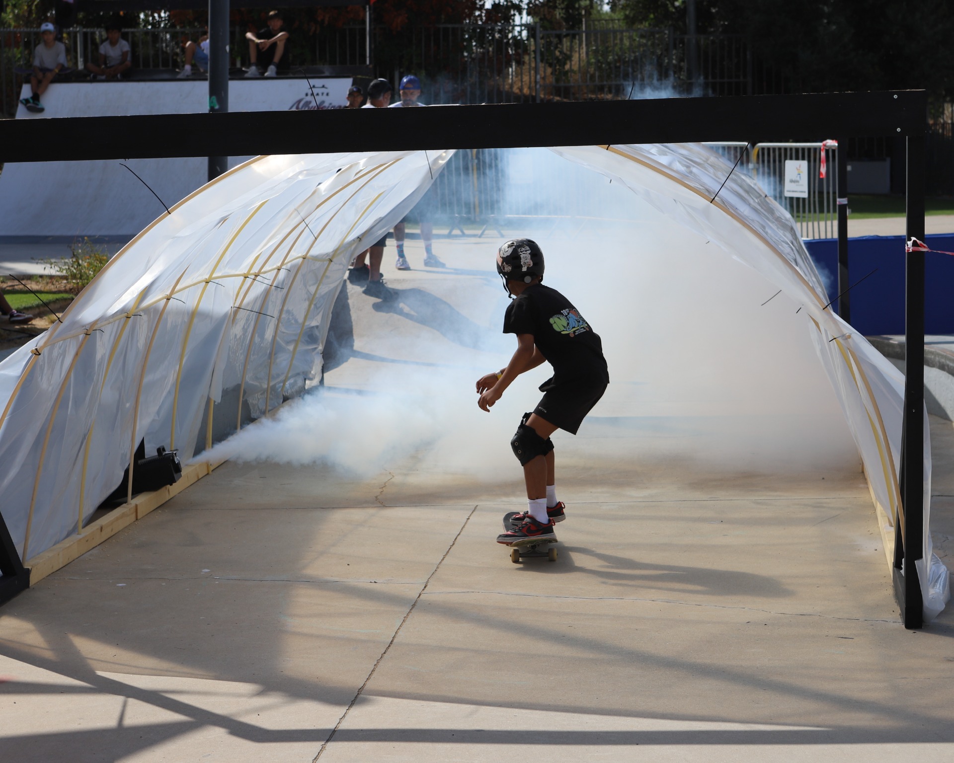 Pessoa de capacete patinando dentro de uma pista coberta com fumaça, sob lona branca e iluminação externa.